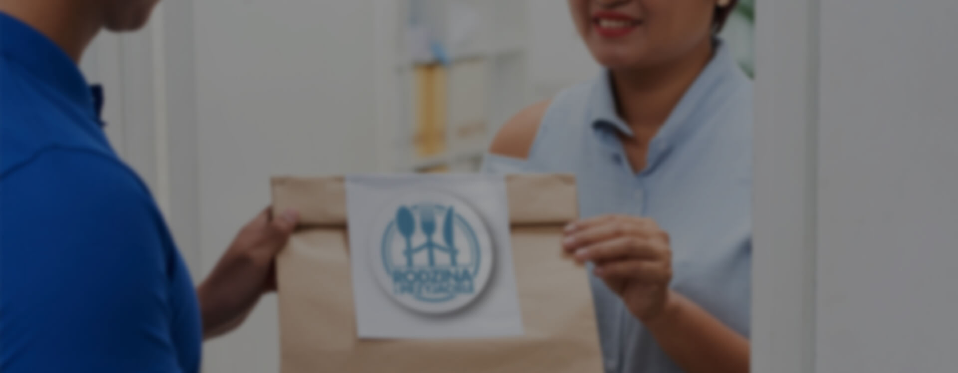 Kobieta wręczająca torbę z jedzeniem na dowóz kobiecie w jasno niebieskiej koszuli.